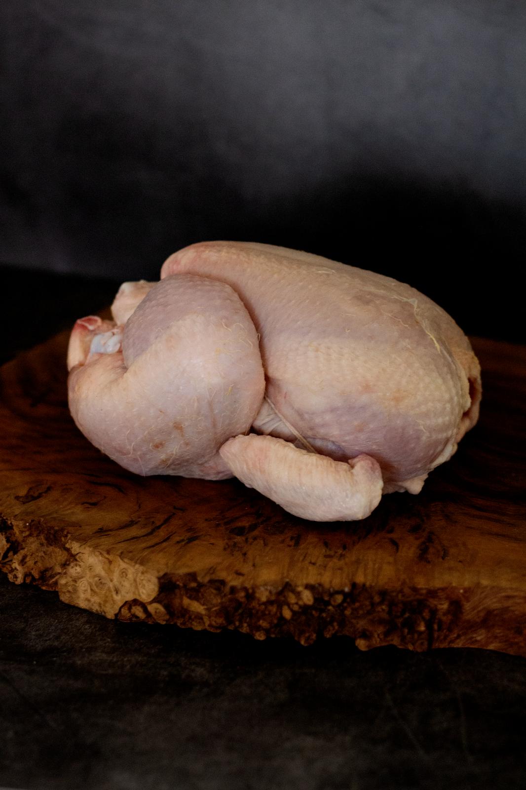 An image showing a whole chicken on a wooden chopping board against a black background.