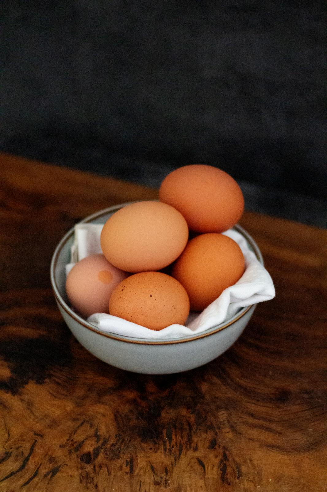 Six eggs in a ceramic bowl, the bowl is placed on a wooden chopping board against a black background.