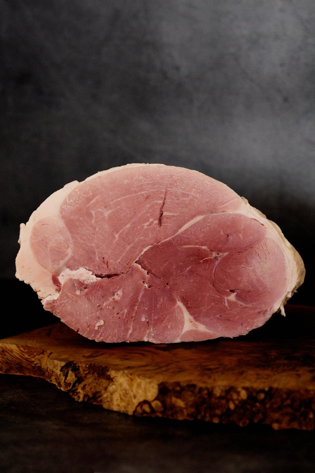 A cooked joint of ham on a wooden chopping board against a black background.