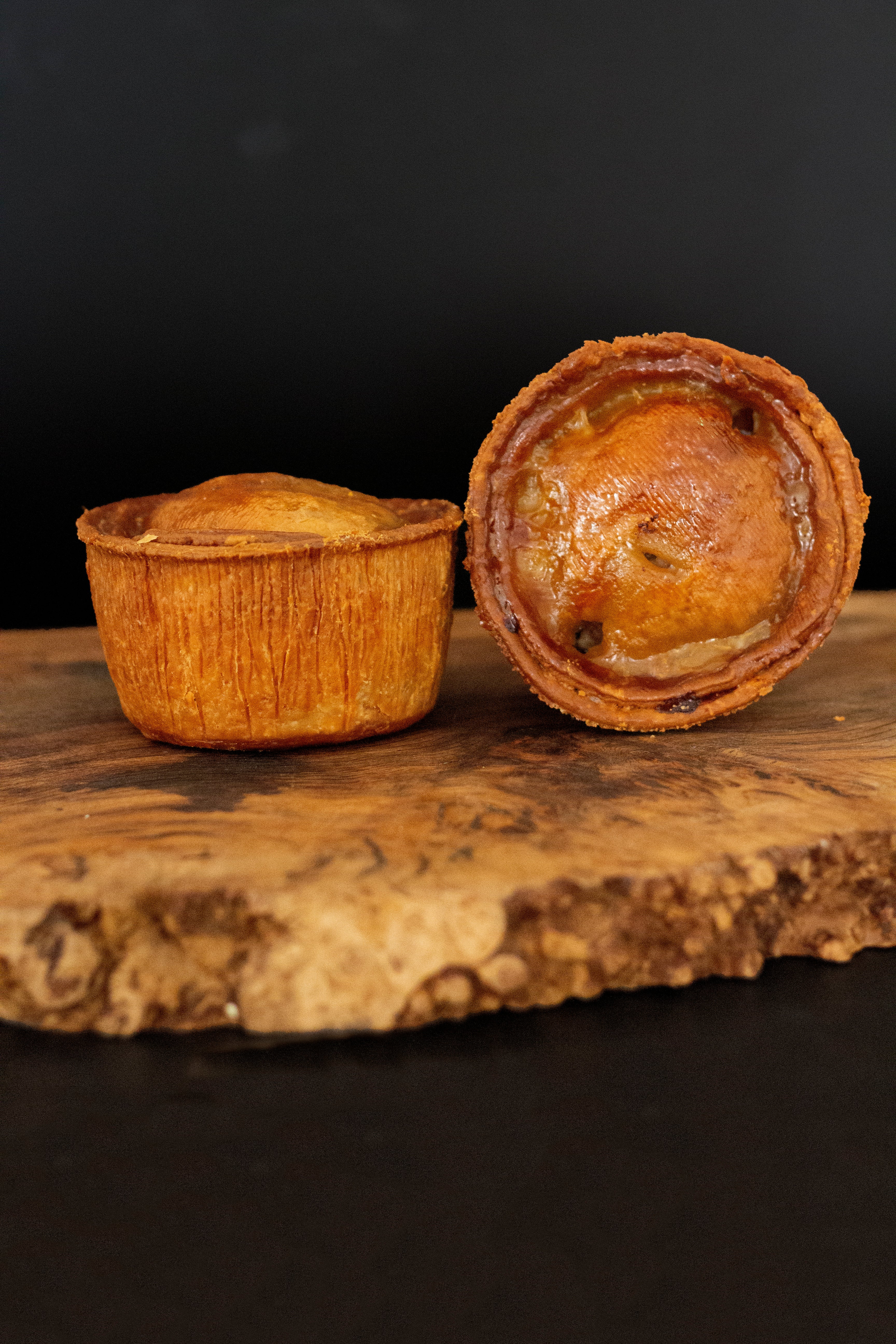 Two large pork pies on a wooden chopping board, against a black background.