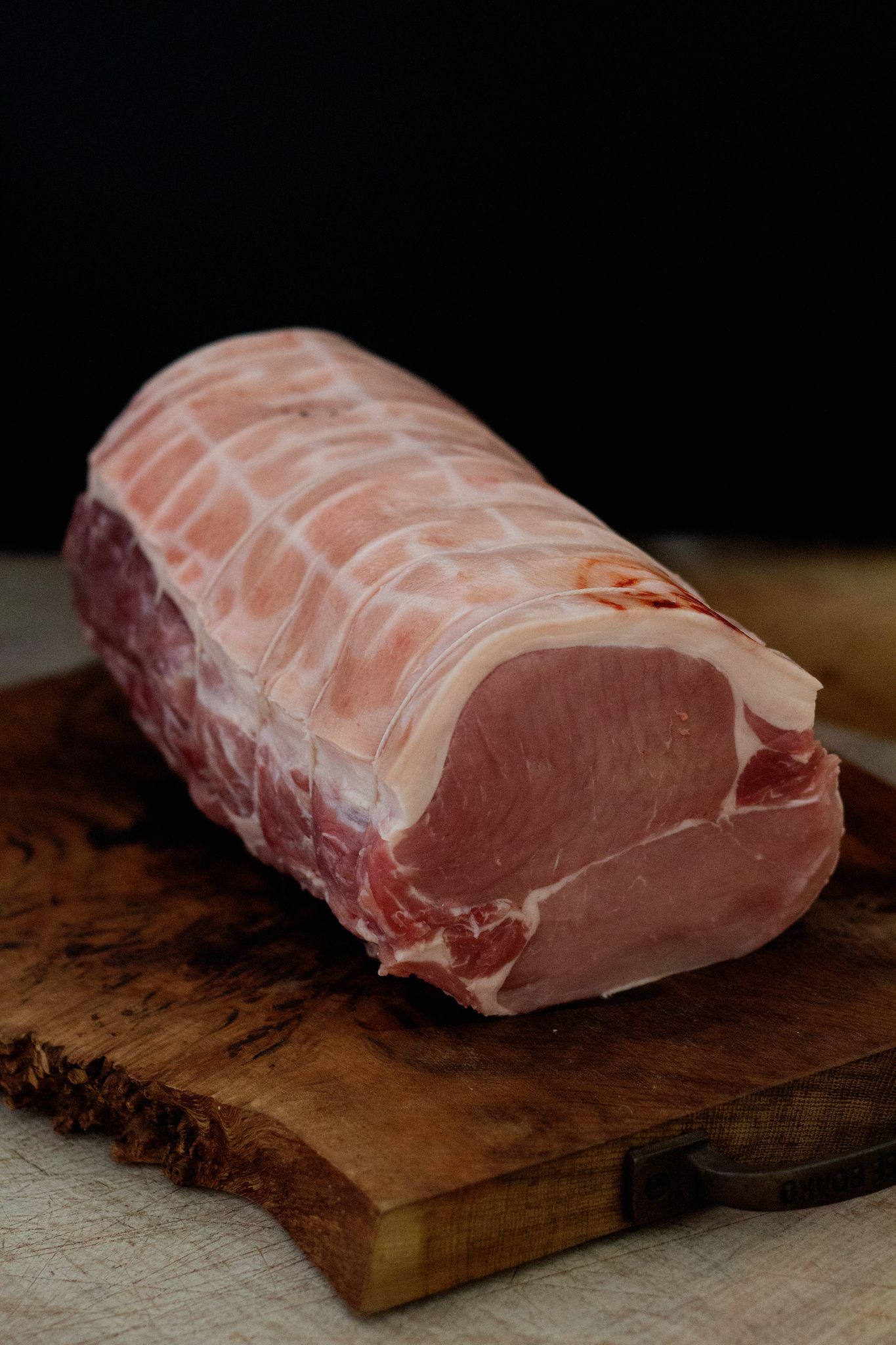 A large pork loin joint on a wooden chopping board, against a black background.