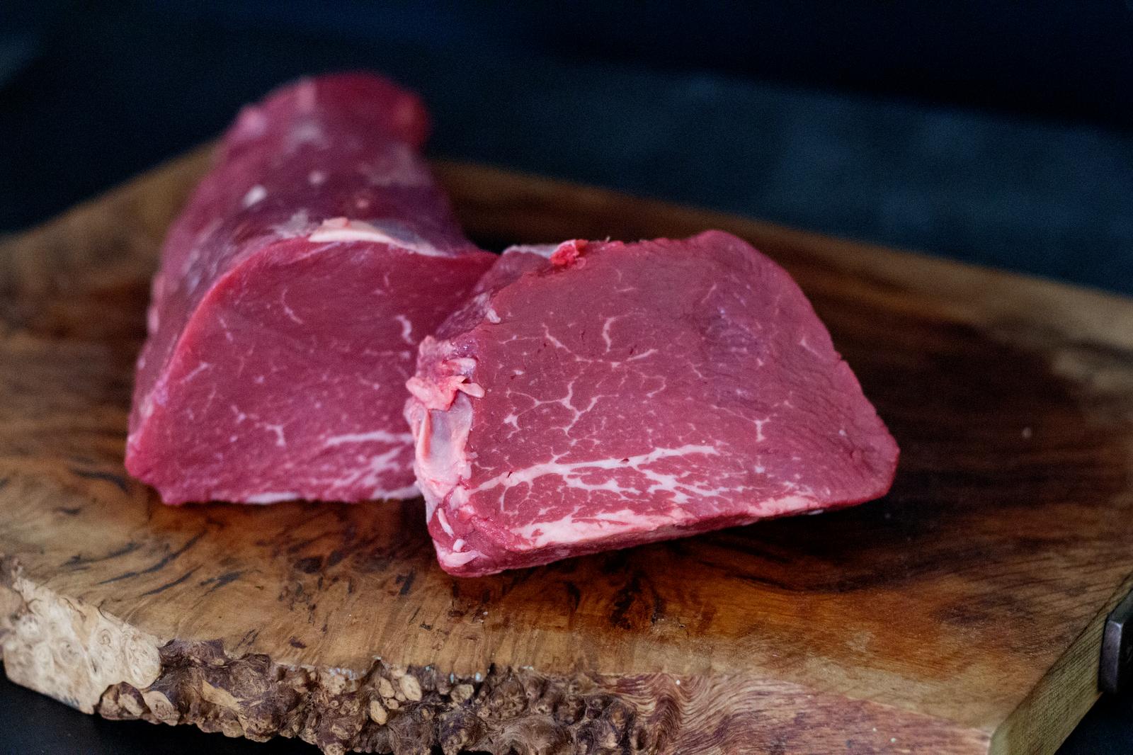 An Image of a fillet steak on a wooden chopping board, with a black background.