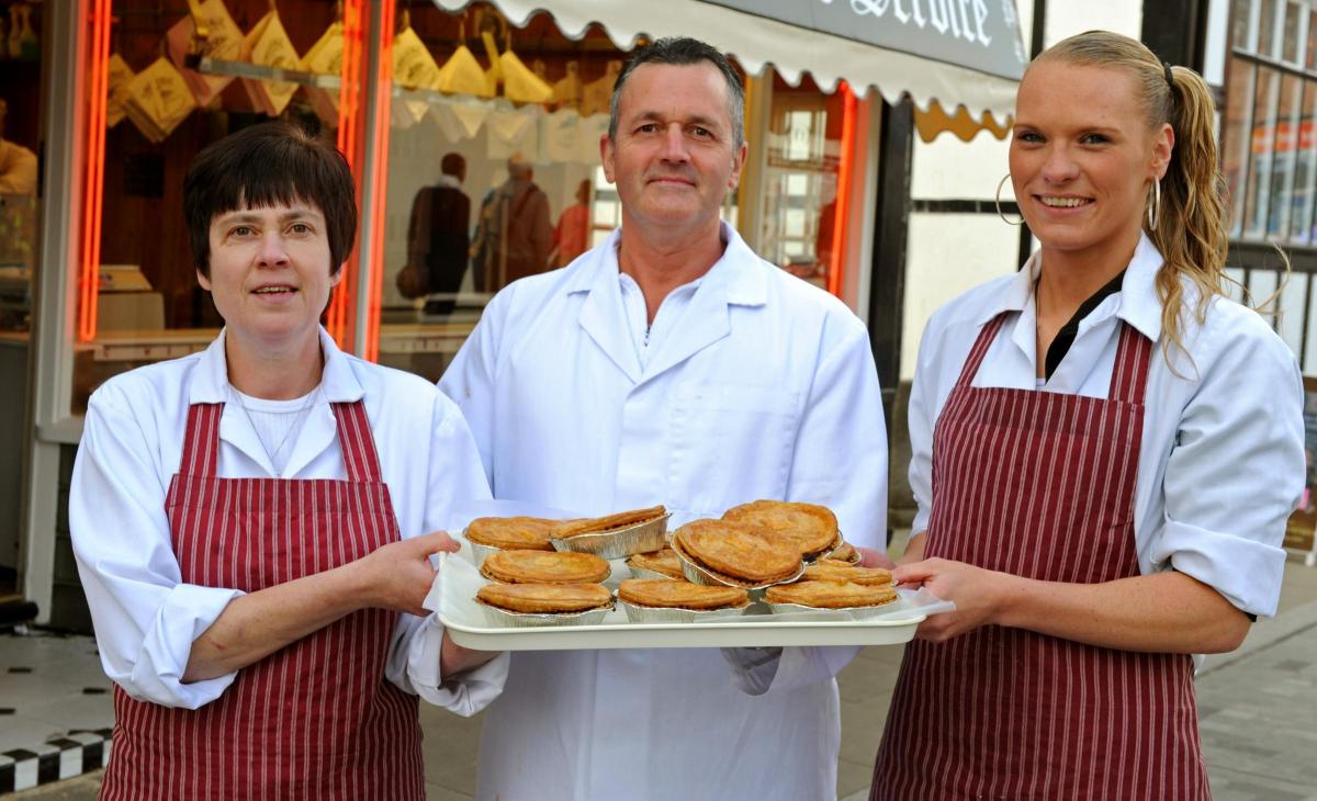 An image of three team members, standing outside the C Webb & Sons shop holding a tray or steak pies.
