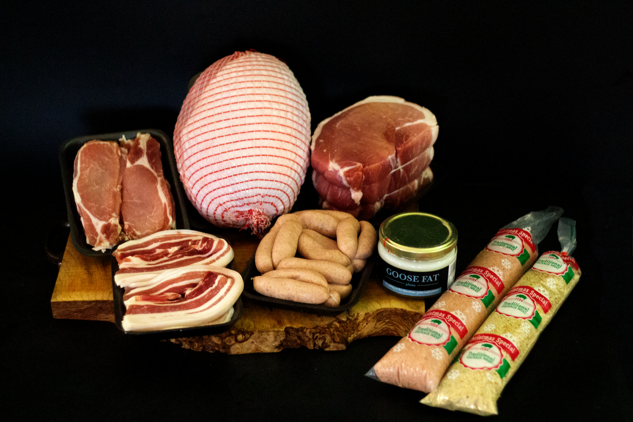 A Christmas meat hamper featuring rolled turkey breast, gammon joint, back bacon, streaky bacon, chipolata sausages, sausage meat, stuffing mixes, and a jar of plain goose fat.